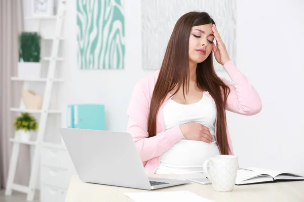 Bela jovem grávida sofrendo de dor de cabeça enquanto trabalhava com laptop em casa — Fotografia de Stock