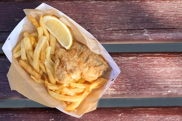 Tasty fried fish and chips with lemon slice on wooden background