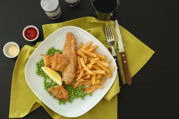 Plaat met lekkere gebakken vis en chips met erwten op tabel — Stockfoto
