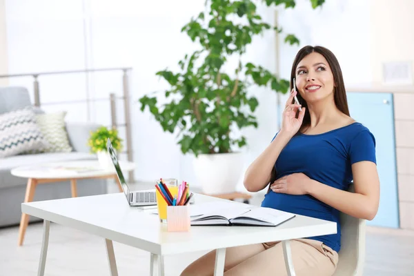 Jeune belle femme enceinte parlant par téléphone tout en travaillant à la maison — Photo