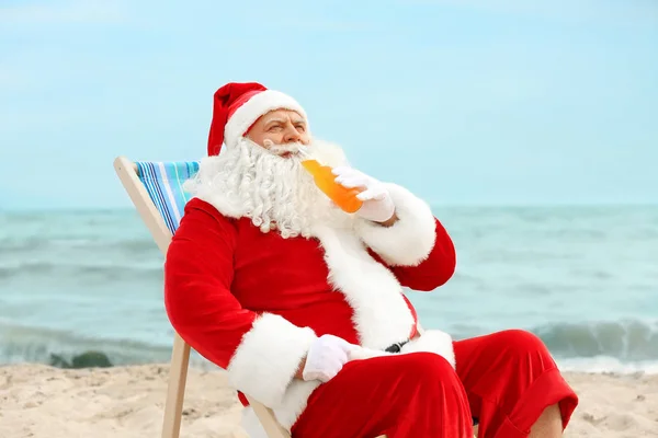 Authentique Père Noël avec bouteille de boisson relaxant dans une chaise longue sur la plage — Photo