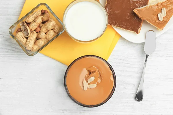 Bowl with delicious peanut butter, glass of milk and toasts on light wooden table — Stock Photo, Image