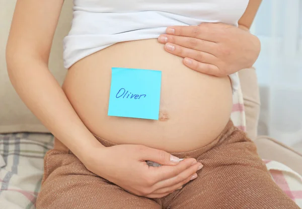 Donna incinta con adesivo di carta sulla pancia, primo piano. Concetto di scegliere il nome del bambino — Foto Stock