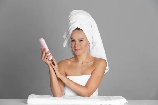 Mulher bonita após o banho com creme corporal no fundo cinza — Fotografia de Stock