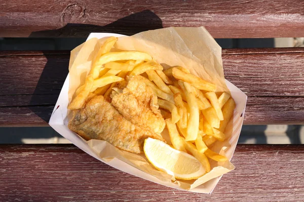 Tasty fried fish and chips with lemon slice on wooden background