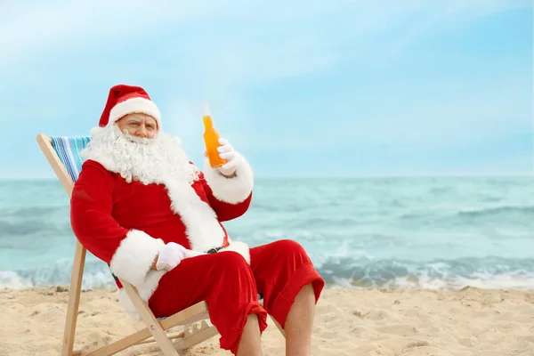 Autêntico Papai Noel com garrafa de bebida relaxante em cadeira de praia — Fotografia de Stock