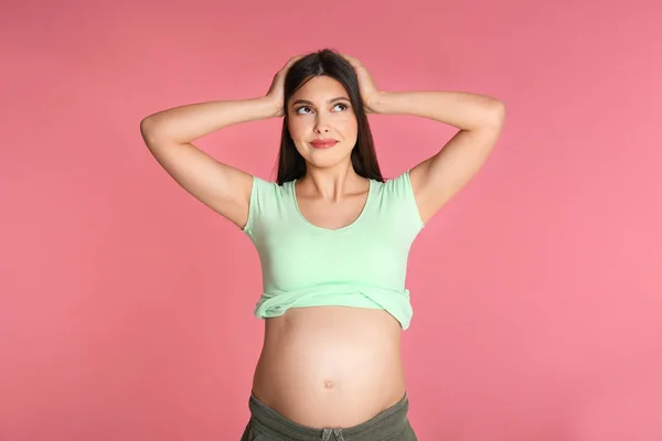 Young pregnant woman choosing name for baby on pink background