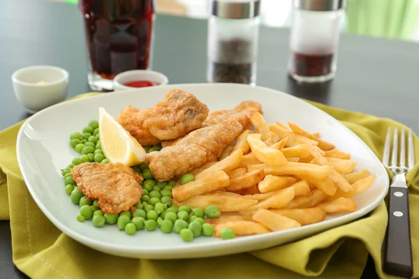 Assiette avec de savoureux poissons frits et des chips avec des pois sur la table — Photo