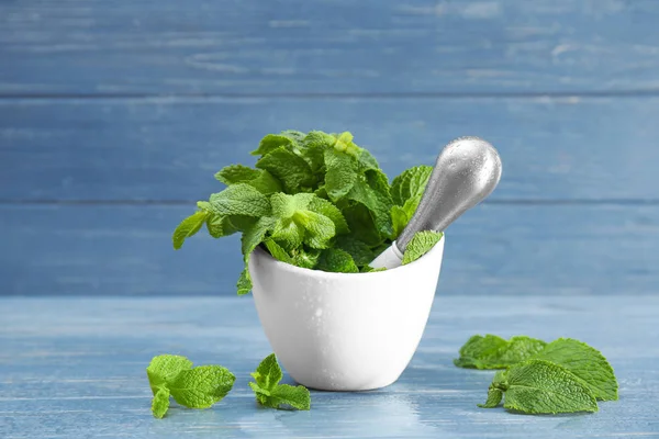 Fresh mint in mortar with pestle on blue wooden background — Stock Photo, Image