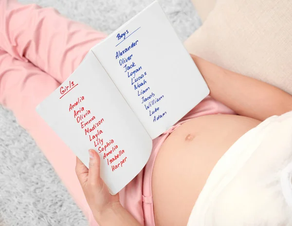 Mulher grávida estudando lista de nomes em casa. Conceito de escolher o nome do bebê — Fotografia de Stock