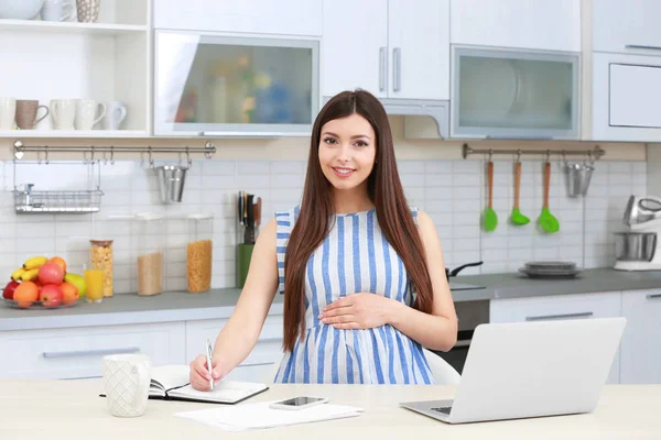 Schöne junge schwangere Frau arbeitet in der Küche — Stockfoto