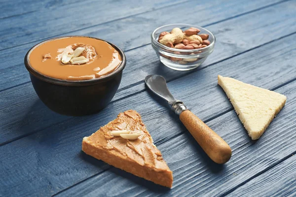 Mangkuk dengan selai kacang lezat, kacang-kacangan dan roti panggang di meja kayu — Stok Foto
