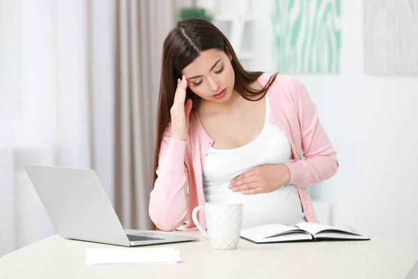 Bela jovem grávida sofrendo de dor de cabeça enquanto trabalhava com laptop em casa — Fotografia de Stock