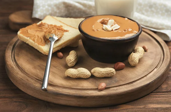 Bowl with delicious peanut butter, toasts and nuts on cutting board — Stock Photo, Image