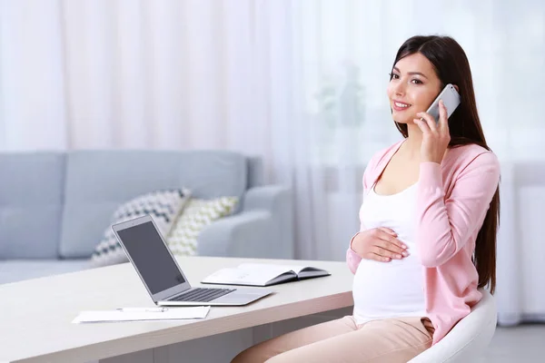 Wanita hamil muda yang sedang berbicara lewat telepon saat bekerja di rumah — Stok Foto