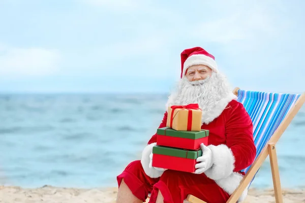 Authentische Weihnachtsmänner mit Geschenkboxen im Liegestuhl am Strand — Stockfoto