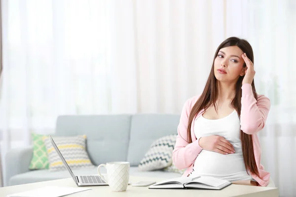 Szép fiatal terhes nő szenved fejfájás, miközben dolgozik a laptop otthon — Stock Fotó