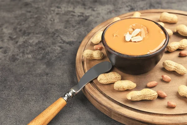 Papan kayu dengan selai kacang lezat, kacang dan pisau di atas meja — Stok Foto