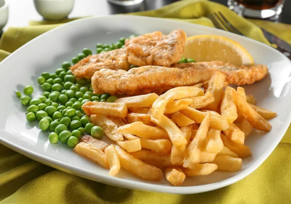 Placa con sabroso pescado frito y patatas fritas con guisantes en la mesa — Foto de Stock