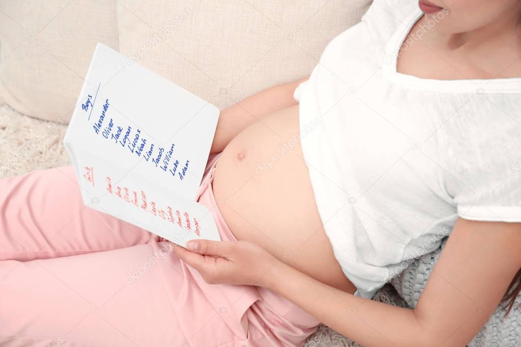 Pregnant woman studying list of names at home. Concept of choosing baby name