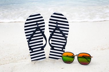 Parmak arası terlik ve plaj kum üzerinde güneş gözlüğü