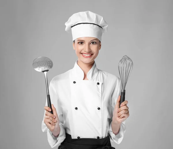 Jovem chef feminino com utensílios sobre fundo claro — Fotografia de Stock