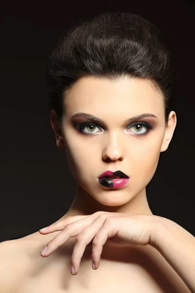 Mooie jonge vrouw met creatieve make-up op donkere achtergrond — Stockfoto