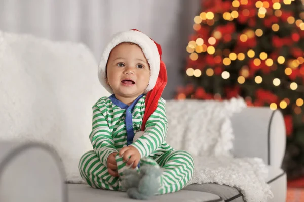 Bebé bonito em chapéu de Papai Noel sentado no sofá decorado para a sala de Natal — Fotografia de Stock