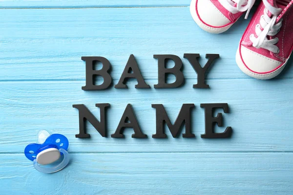 Text Babyname, Schnuller und Schuhe auf farbigem Holzhintergrund — Stockfoto