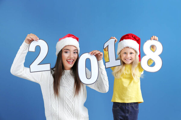 Young woman and cute little girl with paper figures 2018 on color background. Christmas celebration concept