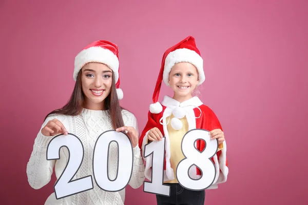 Mujer joven y linda niña con figuras de papel 2018 sobre fondo de color. Concepto de celebración de Navidad —  Fotos de Stock