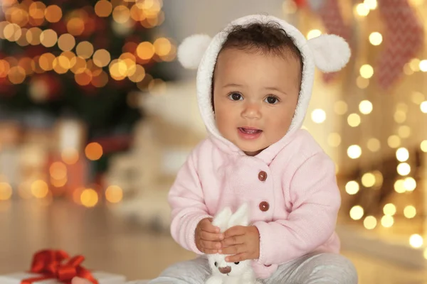 Cute little baby with toy against blurred Christmas lights — Stock Photo, Image