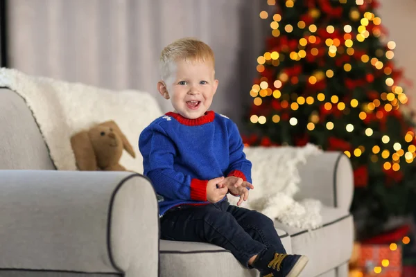 Lindo niño sentado en el sofá en decorado para la habitación de Navidad — Foto de Stock