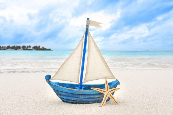 Маленький игрушечный корабль и морская звезда на пляже

