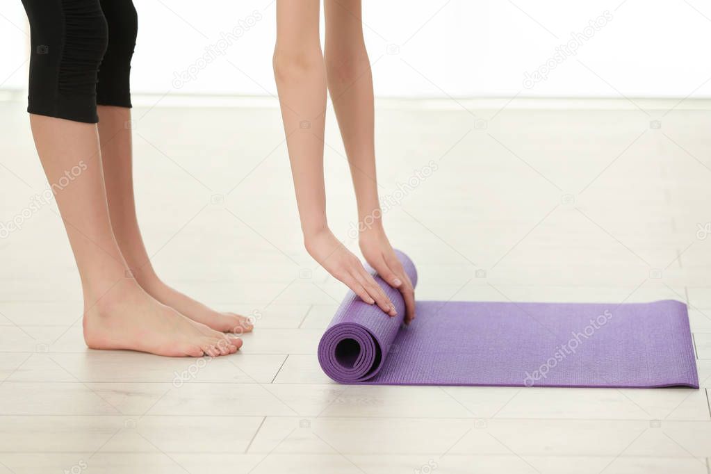 Woman rolling yoga mat on wooden floor