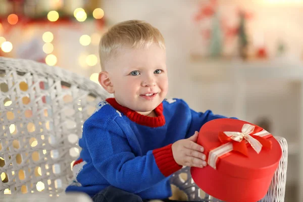 Mignon petit garçon avec boîte cadeau assis dans une chaise en osier sur fond flou — Photo