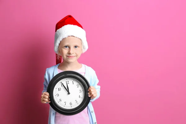 可爱的小女孩，在圣诞老人的帽子，带有时钟的颜色背景。圣诞倒计时概念 — 图库照片