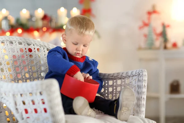 Mignon petit garçon avec boîte cadeau assis dans une chaise en osier sur fond flou — Photo