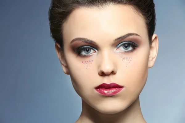 Mooie jonge vrouw met creatieve make-up op kleur achtergrond — Stockfoto