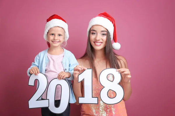 Mujer joven y linda niña en sombreros de Santa con figuras de papel 2018 sobre fondo de color. Concepto de celebración de Navidad —  Fotos de Stock