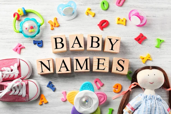 Würfel mit Text Babynamen, Spielzeug, Schnuller, Plastikbuchstaben und Schuhe auf Holzgrund — Stockfoto