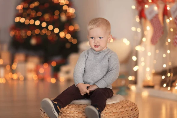 Lindo niño sentado en la silla otomana en decorado para la habitación de Navidad — Foto de Stock