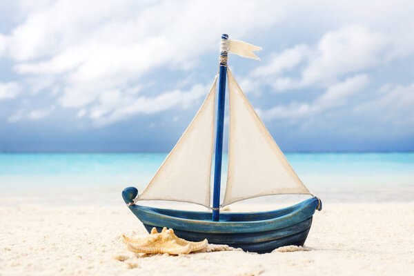 Игрушечный корабль и морская звезда на песке у моря
