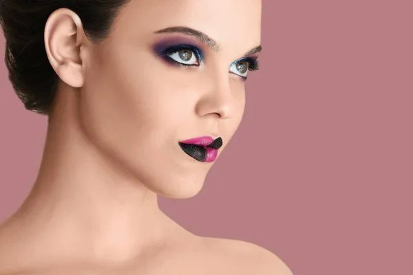 Mooie jonge vrouw met creatieve make-up op kleur achtergrond — Stockfoto