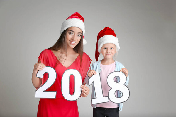 Young woman and cute little girl in Santa hats with paper figures 2018 on light background. Christmas celebration concept