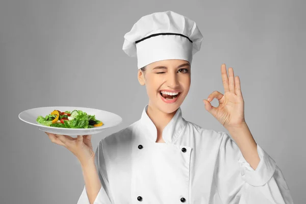 Jovem chef feminino segurando prato com salada no fundo claro — Fotografia de Stock