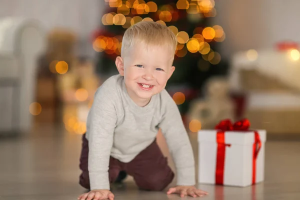 Netter kleiner Junge mit Geschenkbox auf dem Boden vor verschwommenem Hintergrund — Stockfoto