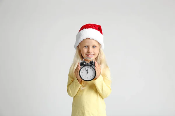 Ragazzina carina a Babbo Natale con orologio su sfondo chiaro. Conto alla rovescia di Natale — Foto Stock