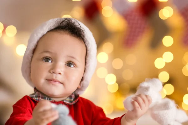 Bebê bonito em chapéu de Papai Noel contra luzes de Natal borradas — Fotografia de Stock