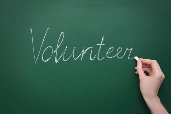 Женщина пишет слово VOLUNTEER на зеленой доске
